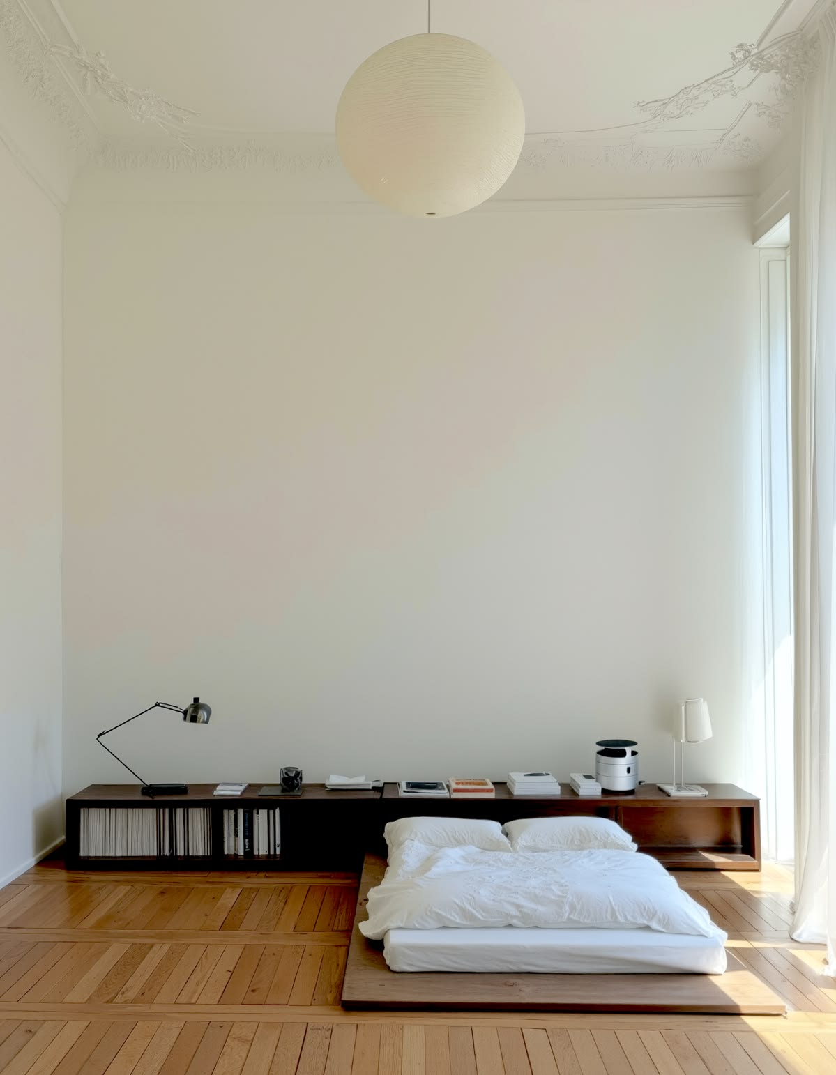 A minimalist bedroom with a low futon bed, wooden floor, and pendant paper lamp